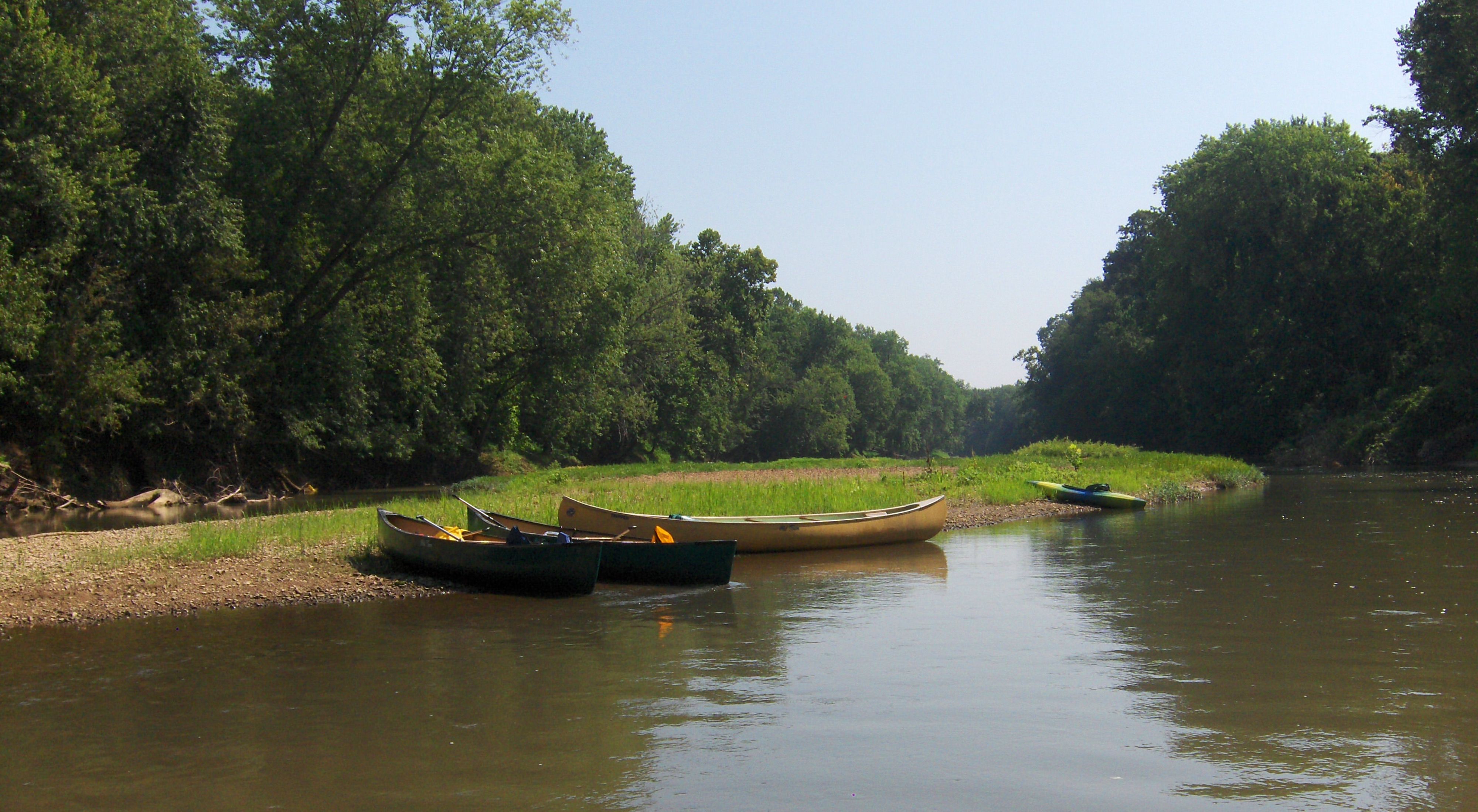 Three canoes and a kayak sit on the side of a river bank.