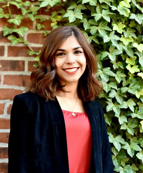 Humna Sharif poses for a headshot standing outdoors in front of an ivy covered brick wall.