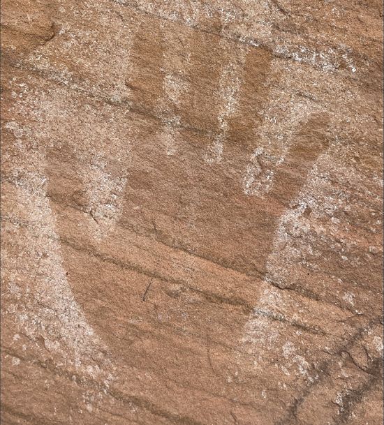 An outline of a human hand on the surface of a sandstone cliff wall.