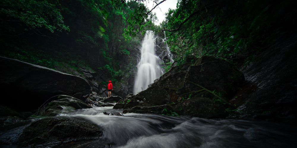 A person stands in front of a magnificent waterfall.
