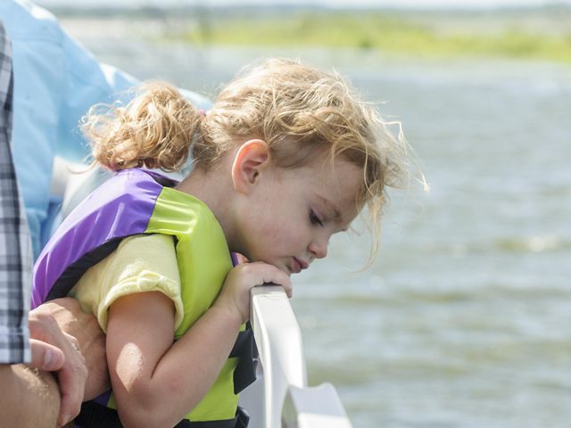Girl wearing lifejacket stares over edge of a boat down at the water on a sunny day on a lake.