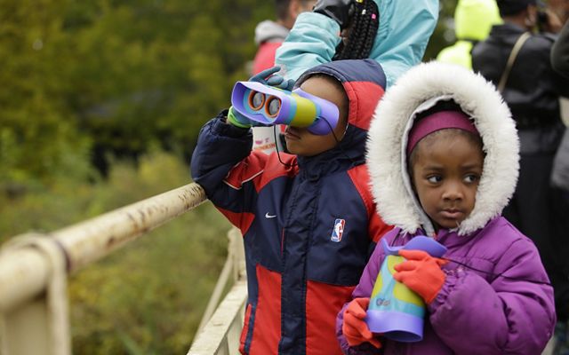 2 niños pequeños en un parque de Chicago miran a través de unos binoculares hechos específicamente para niños.