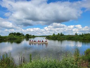 A group of people in a ten-person canoe on the water as seen from the bank at Emiquon.