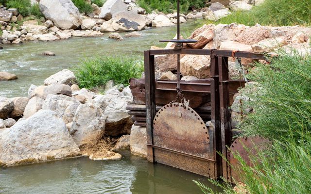 An old, rusty headgate that controls water flowing through a river.