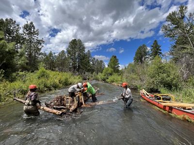 A work crew is gathering logs in a river.