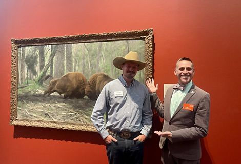Two men, one wearing a cowboy hat and the other a bowtie, smile for a photo together.