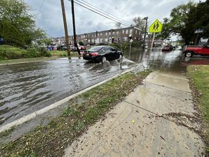 A car drives through a flooded residential street. 