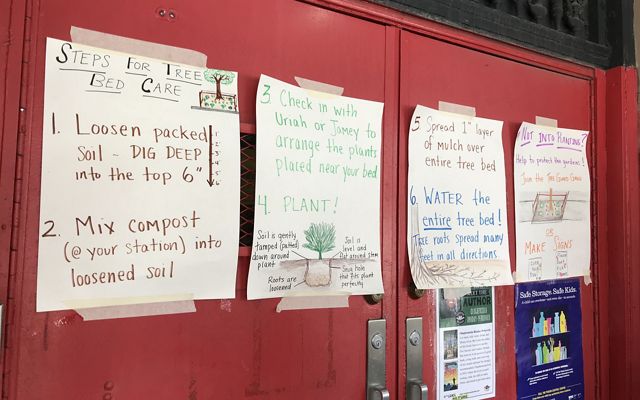 Three hand-written signs of instructions for tree stewardship and care are taped to a wall of red lockers.