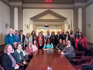 A group of people gather around the end of a table in Delaware's legislative hall and smile and the camera. 
