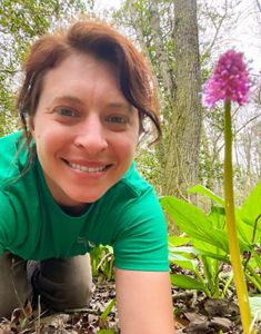 A person leaning down onto the ground and taking a selfie with a pink flower.