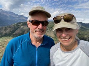 Two people pose together in front of a rolling mountain ridge.