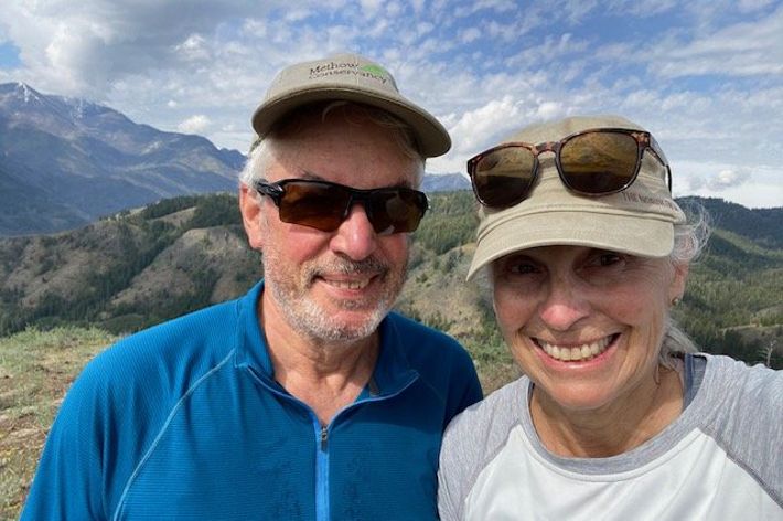 Two people pose together in front of a rolling mountain ridge.