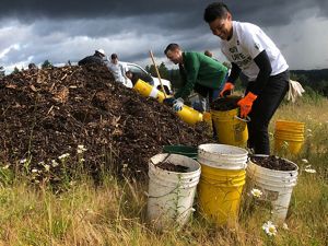 Several volunteers with work gloves and buckets by a pile of dirt with a white pick up truck.