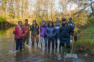 A group of Nature Conservancy staff stand in shallow creek on sunny fall day.