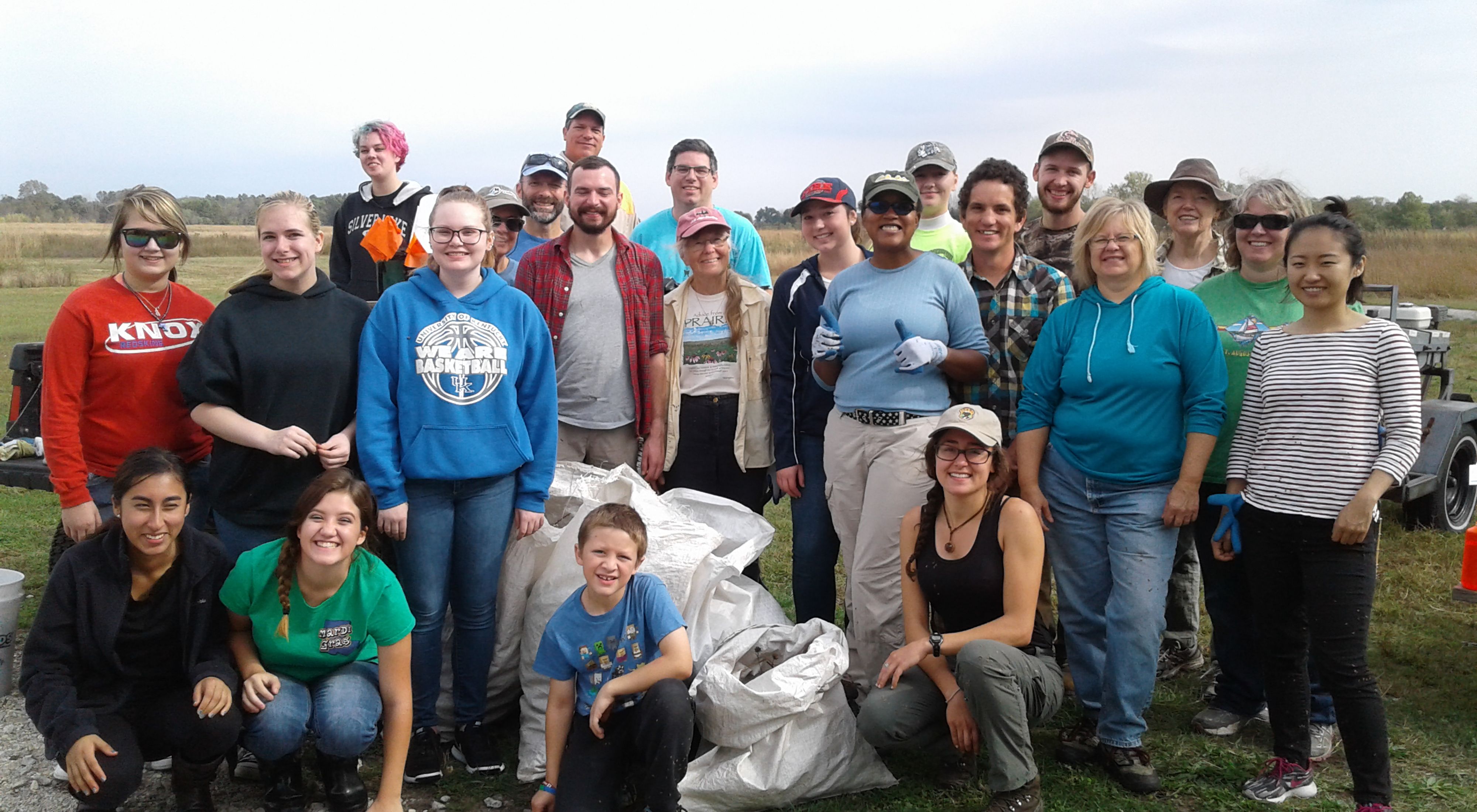 Large group of volunteers with a giant white bag of collected prairie seed.
