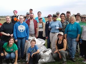 Large group of volunteers with a giant white bag of collected seed.