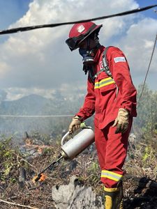 A person in a red jumpsuit uses a torch to start a fire.