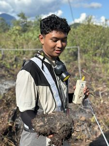 A person holds a chunk of soil in one hand and a piece of equipment in the other hand.