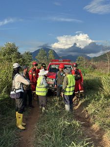A group of people gather next to a red fire truck in the middle of a natural area.