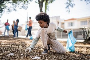 A boy kneels down in mulch to pick up a piece of trash.