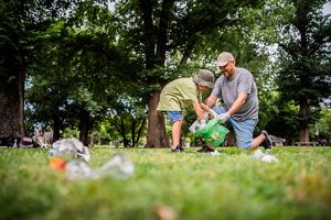A child and adult bend over in a grassy area to pick up trash.