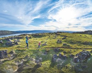 A family runs on a hiking path with a scenic Oregon vista in the background with a river and Mount Hood in the background.