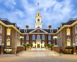 Dramatic view of the Delaware state capitol building. White clouds hang low over the colonial-style state house that features a tall spire rising above the front entrance.