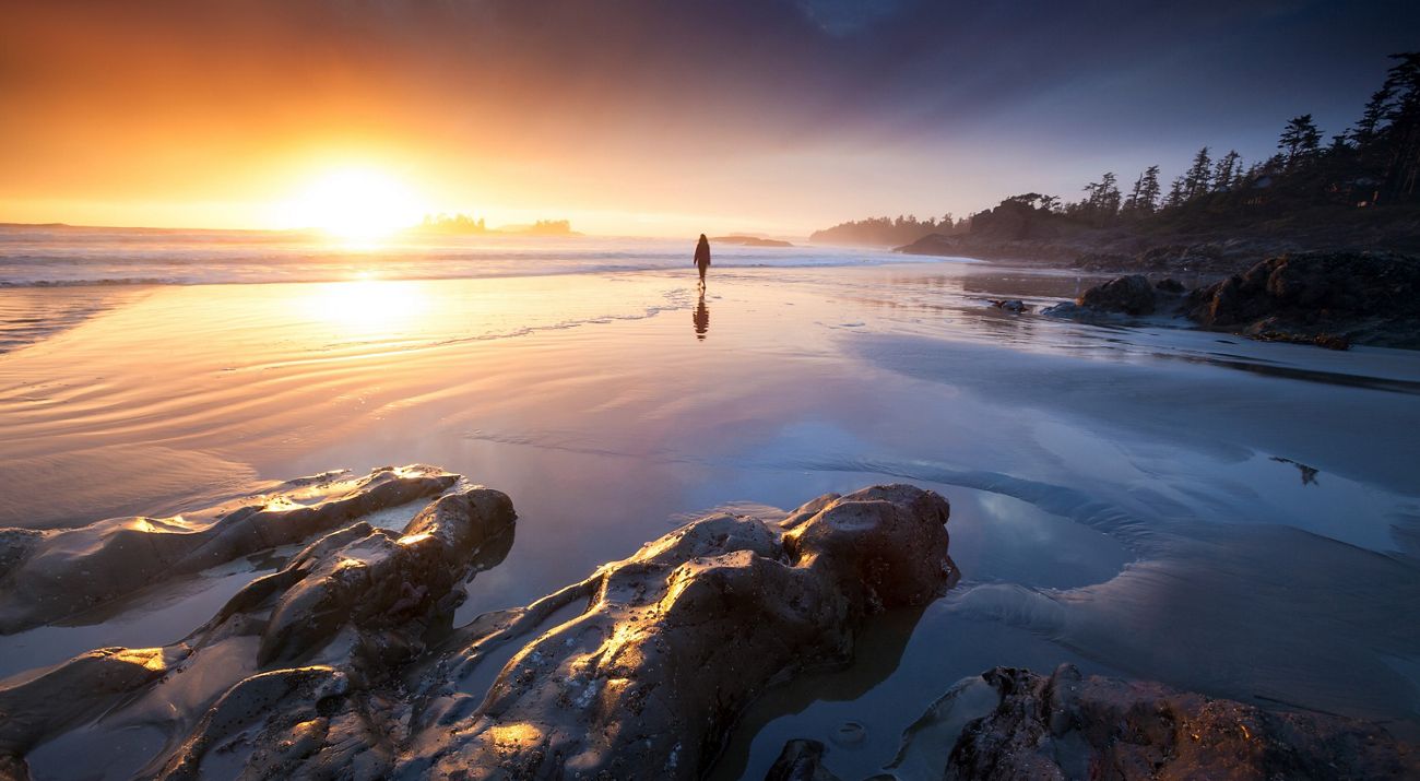Person standing on a beach at sunset.