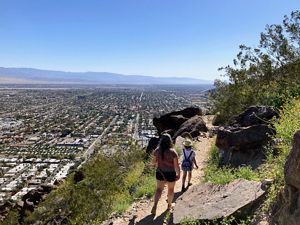 A mom and daughter admiring the beautiful view of the coachella valley and all the surrounding cities hiking high above. Views of the desert and mountains are clear on a beautiful sunny day.