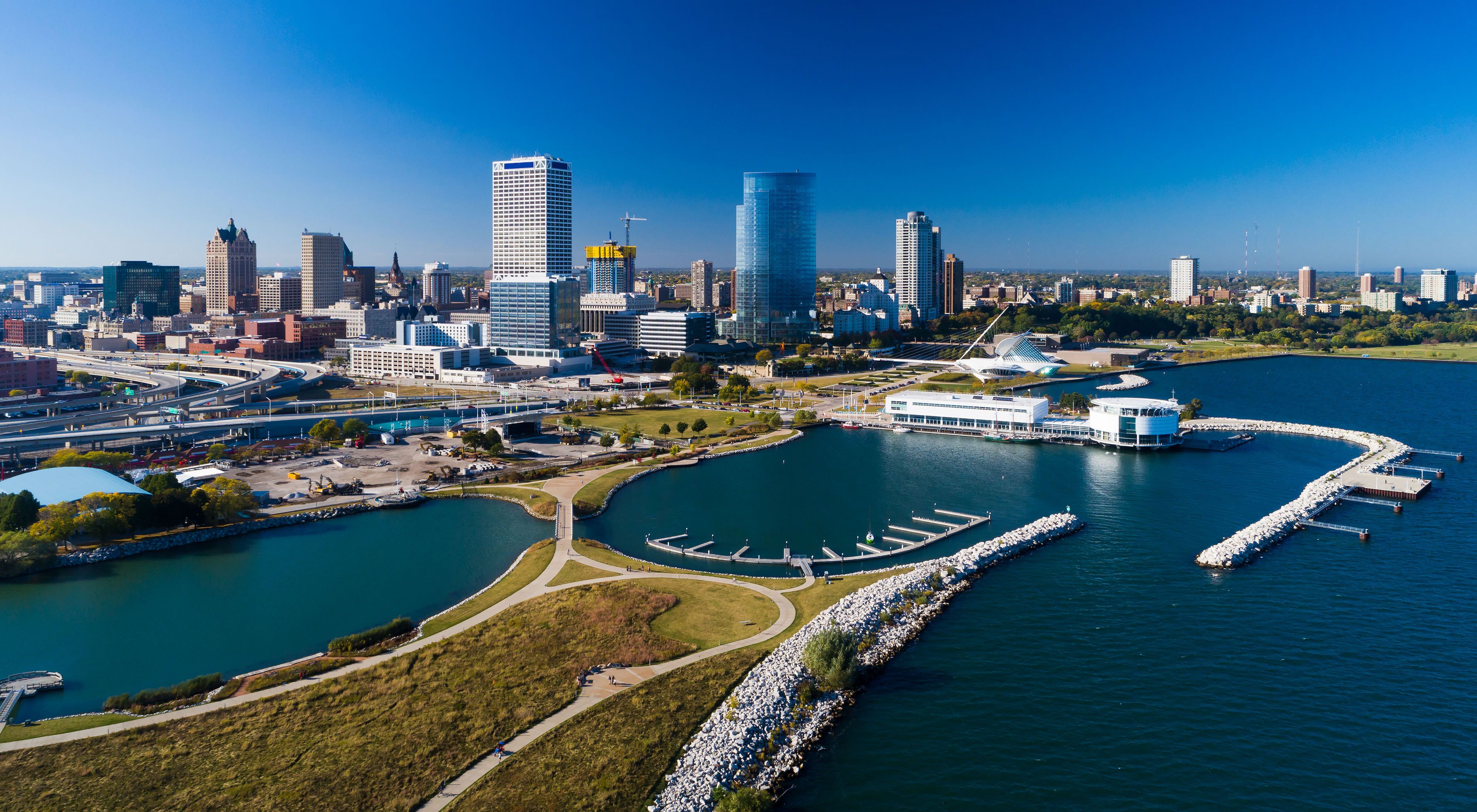 Aerial image of Milwaukee skyline on a blue sky day with Discovery World and Lakeshore State Park in the foreground.