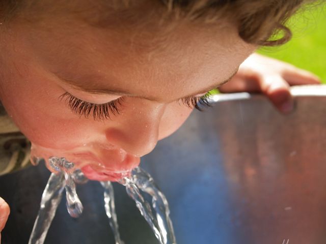 A child drinking from a spurt of water from a fountain.