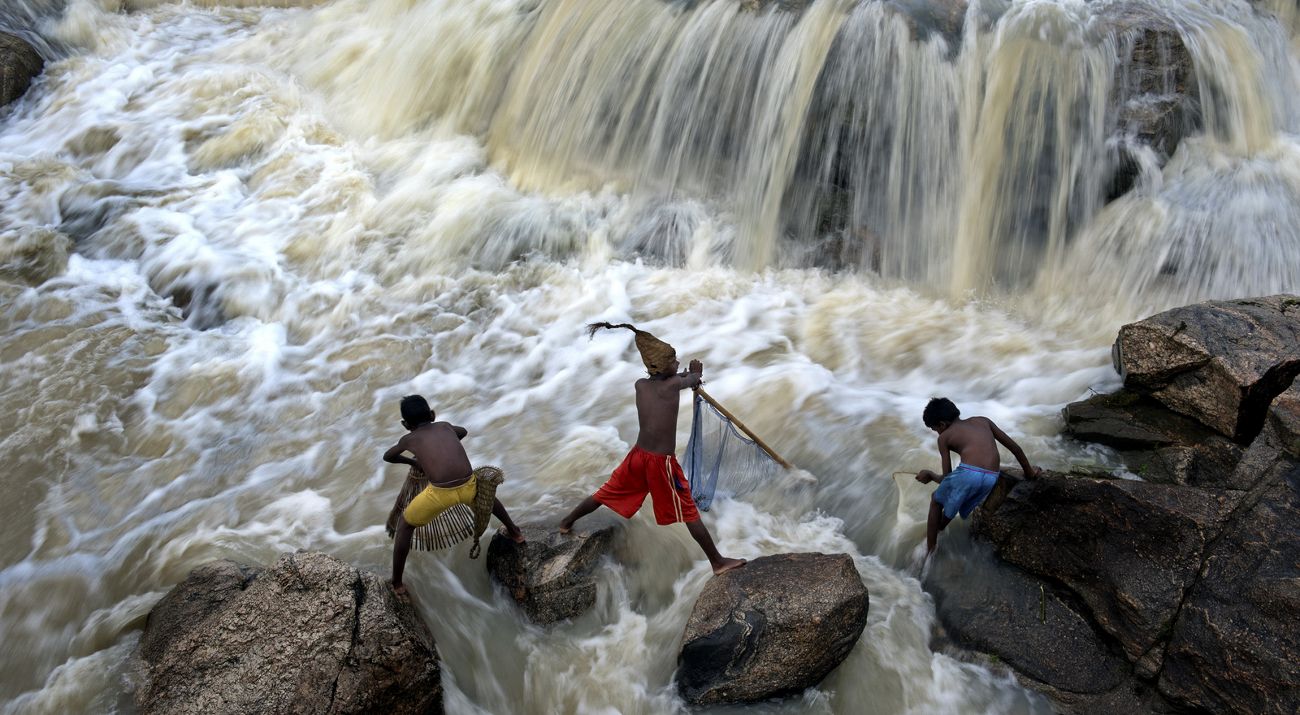 3 kids play on rocks in river