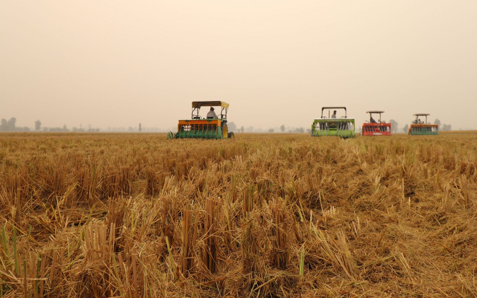 four plows drive through a brown field against a smoggy sky