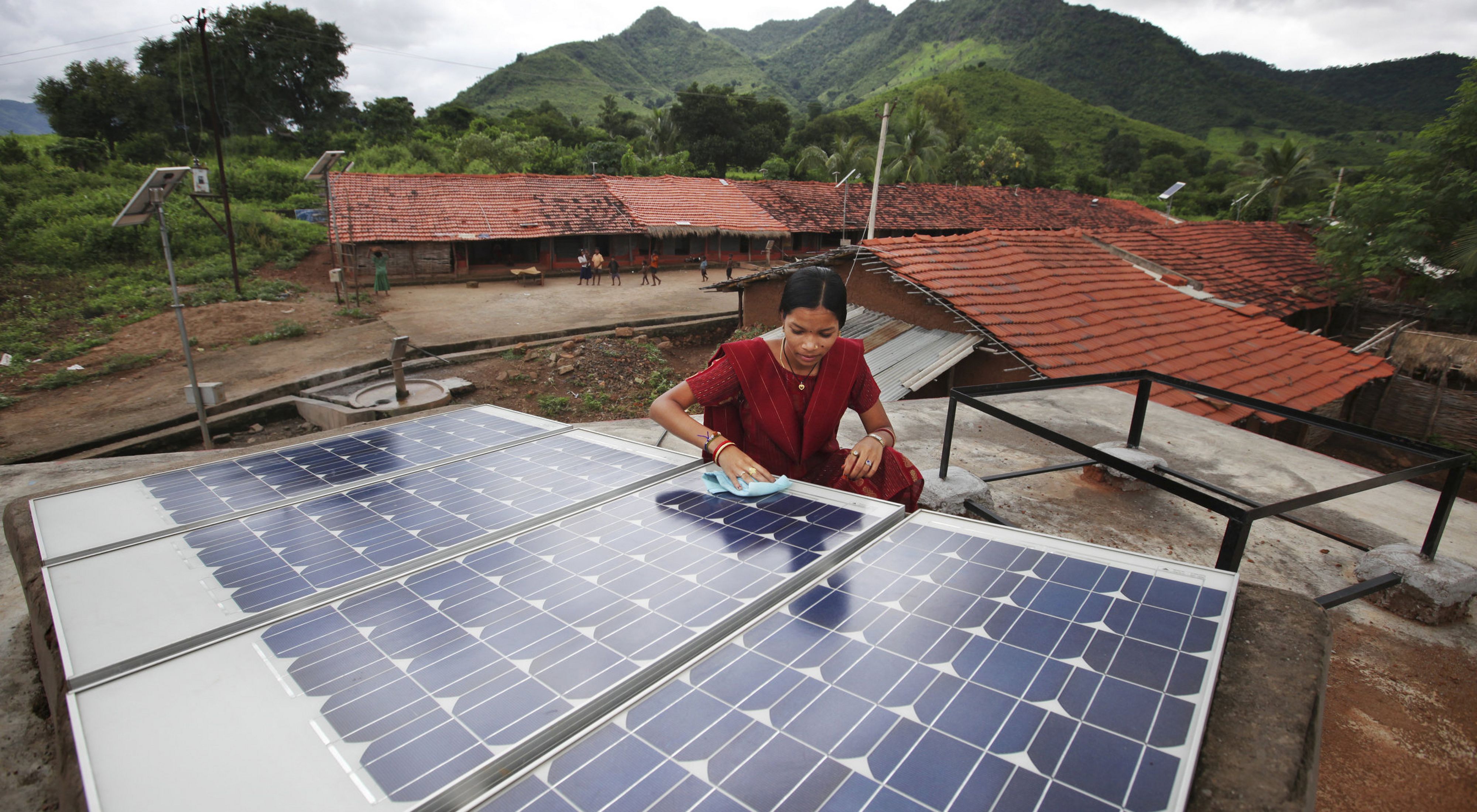 A person uses a cloth to clean solar panels on the roof of a village home in India.