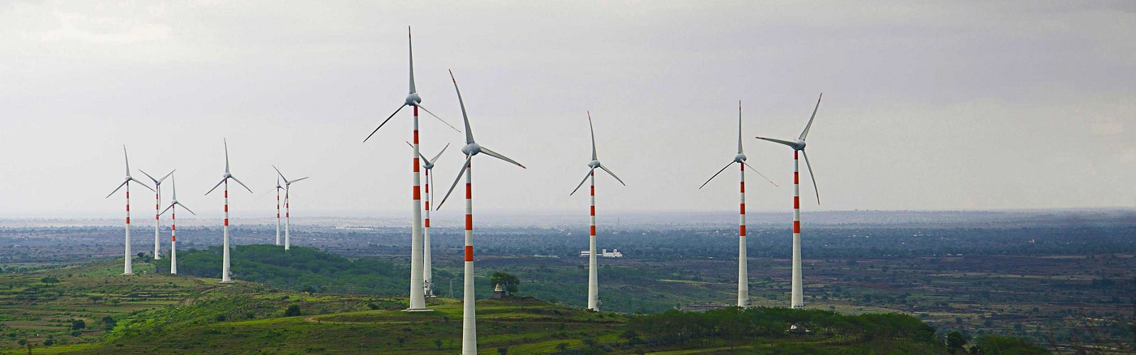 Several white wind turbines with red stripes stand in a vast green landscape in India.