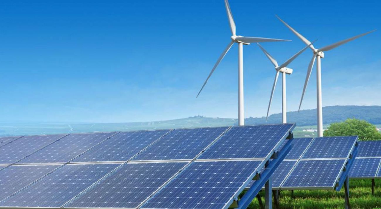 Wind turbines stand behind solar panels in a landscape.