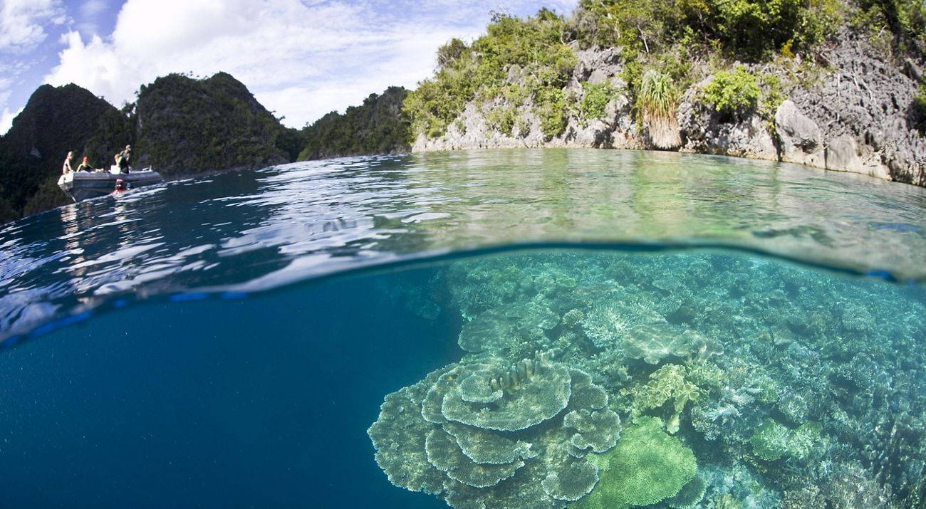 A boat of divers explores the shallow fringing reefs of a remote limestone island just off Misool Island. Raja Ampat, Papua, Indonesia.