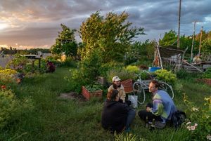 Three people sitting in a garden next to a bicycle.