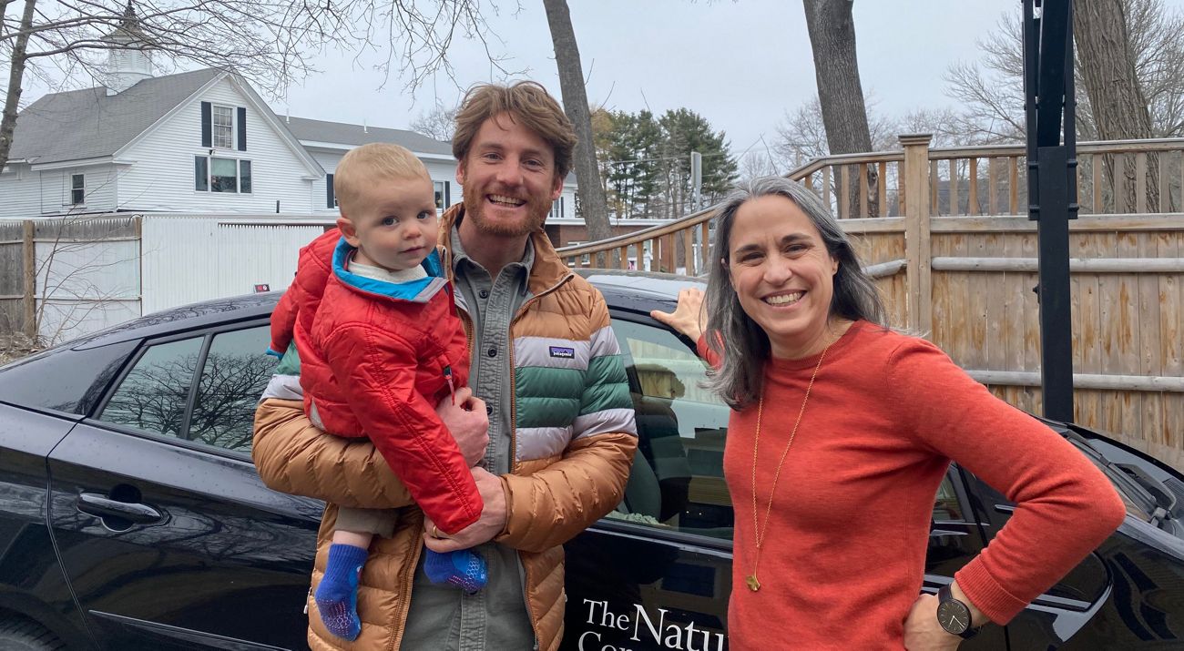 A smiling man holds a young child and stands next to a smiling woman.