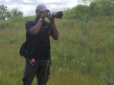 Our fellow Jajuan takes a picture with a large camera while standing in a field of prairie grass.