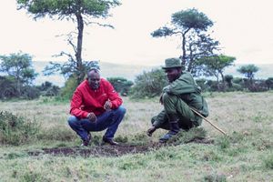 Two men kneel in a Kenya grassland.