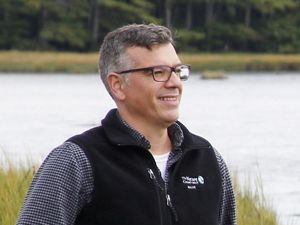 Jeremy Bell looks off to the distance with grasses and water behind him.