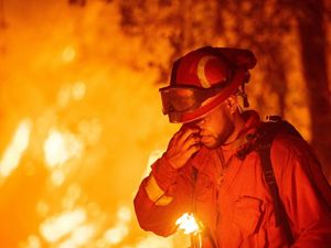 A firefighter wipes his eyes as he stands in front of a burning house.