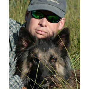 Headshot of Jeffrey Evans in ballcap and sunglasses, with his dog.