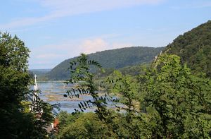 View through tree branches of the Potomac River as it winds between green mountains and the town of Harpers Ferry.