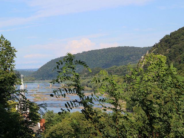 View through tree branches of the Potomac River as it winds between green mountains and the town of Harpers Ferry.
