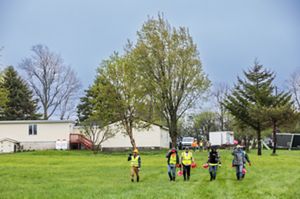A group of people on land with a tree wearing bright vests and planting tools. 