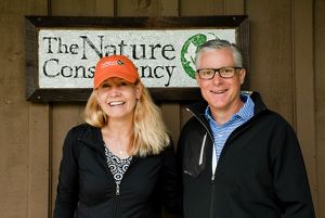 Two people stand in front of a building smiling at the camera.