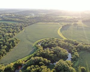 Aerial view of a river, crop field and forest with the sunset in the background.