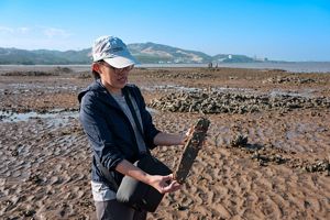 A woman holding a concrete pole in a mudflat.